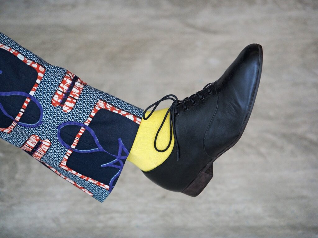 A man with colorful pants takes a big step with a yellow sock and black dress shoes